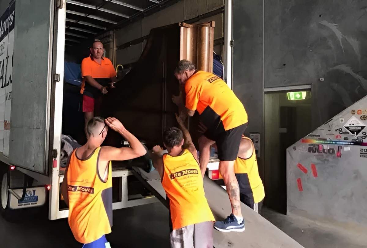Movers in Orange Shirts Load a Large, Dark Piece of Furniture — Lite Moves Furniture Removals In Sydney, NSW