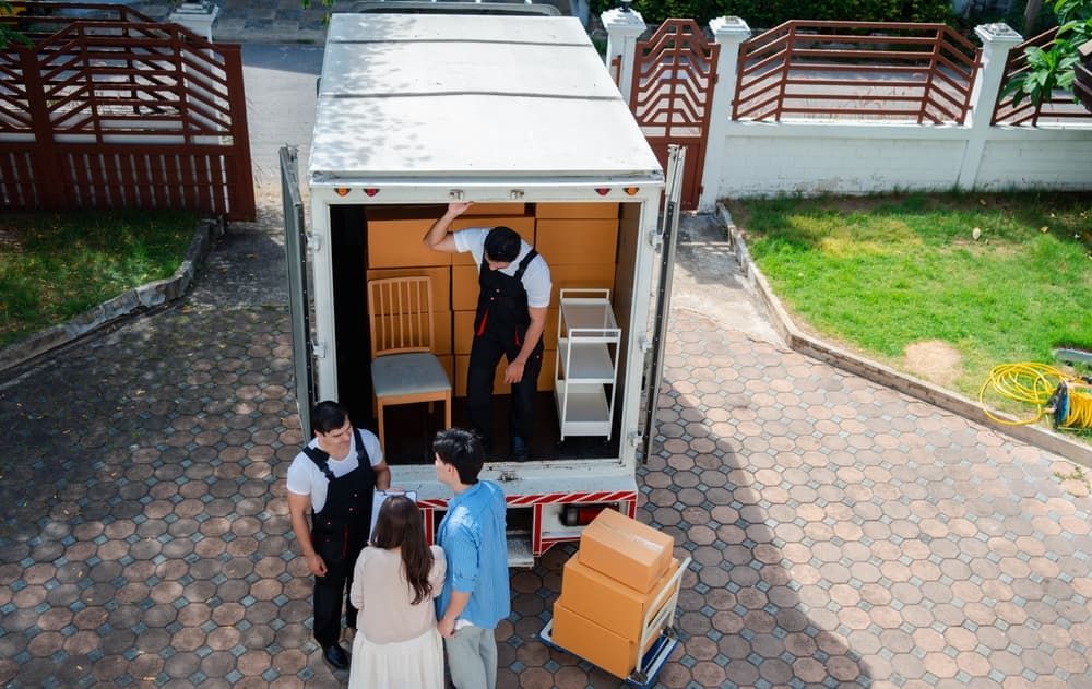 Movers Loading A Truck With Boxes And Furniture In Front Of A House