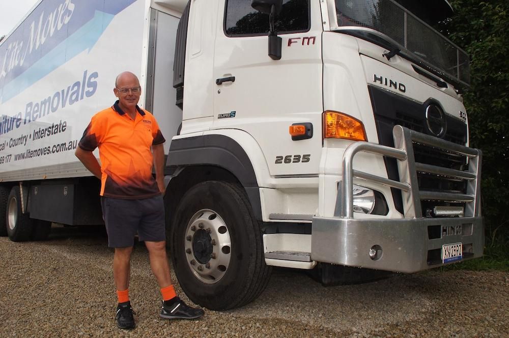 A Man in an Orange Work Shirt and Shorts Stands — Lite Moves Furniture Removals In Sydney, NSW