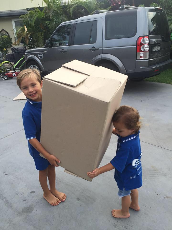 Two Young Boys Are Carrying a Large Cardboard Box — Lite Moves Furniture Removals In Sunshine Coast, NSW