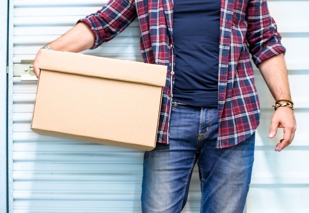 Man Holding A Moving Cardboard Box In Front Of A Storage Door — Lite Moves Furniture Removals In Bonville, NSW