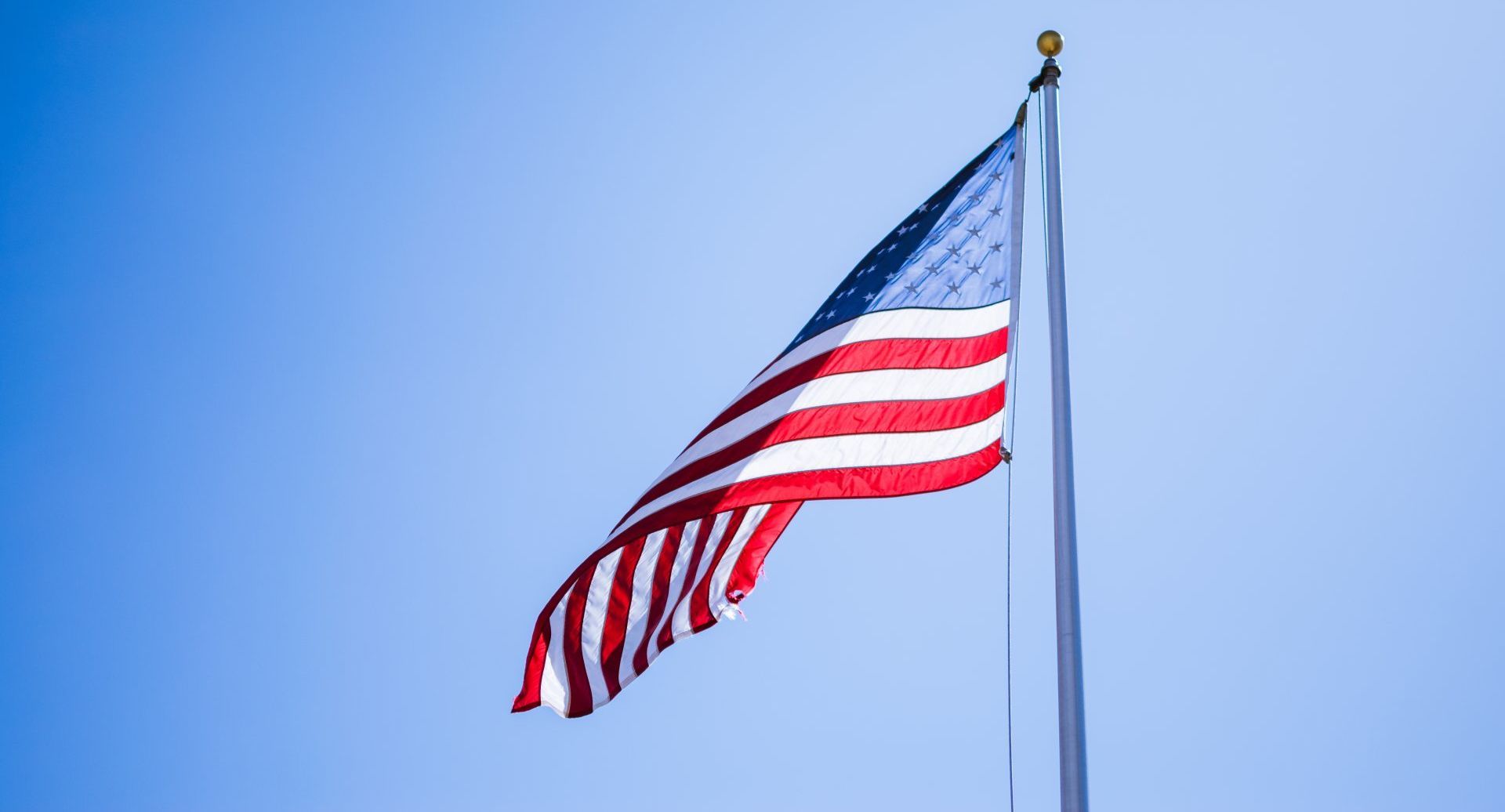 An american flag is waving in the wind against a blue sky.