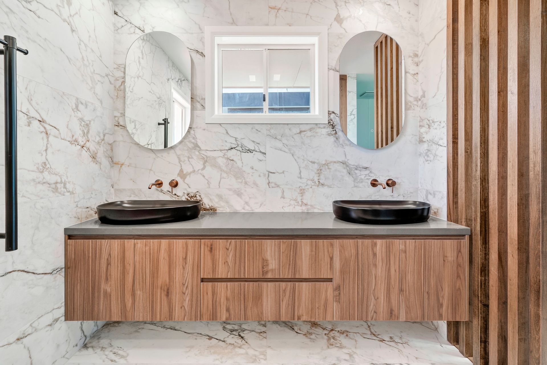Bathroom with wood-look vanity, marble walls, oval mirrors, and black sinks — PK4 Projects in Port Macquarie, NSW