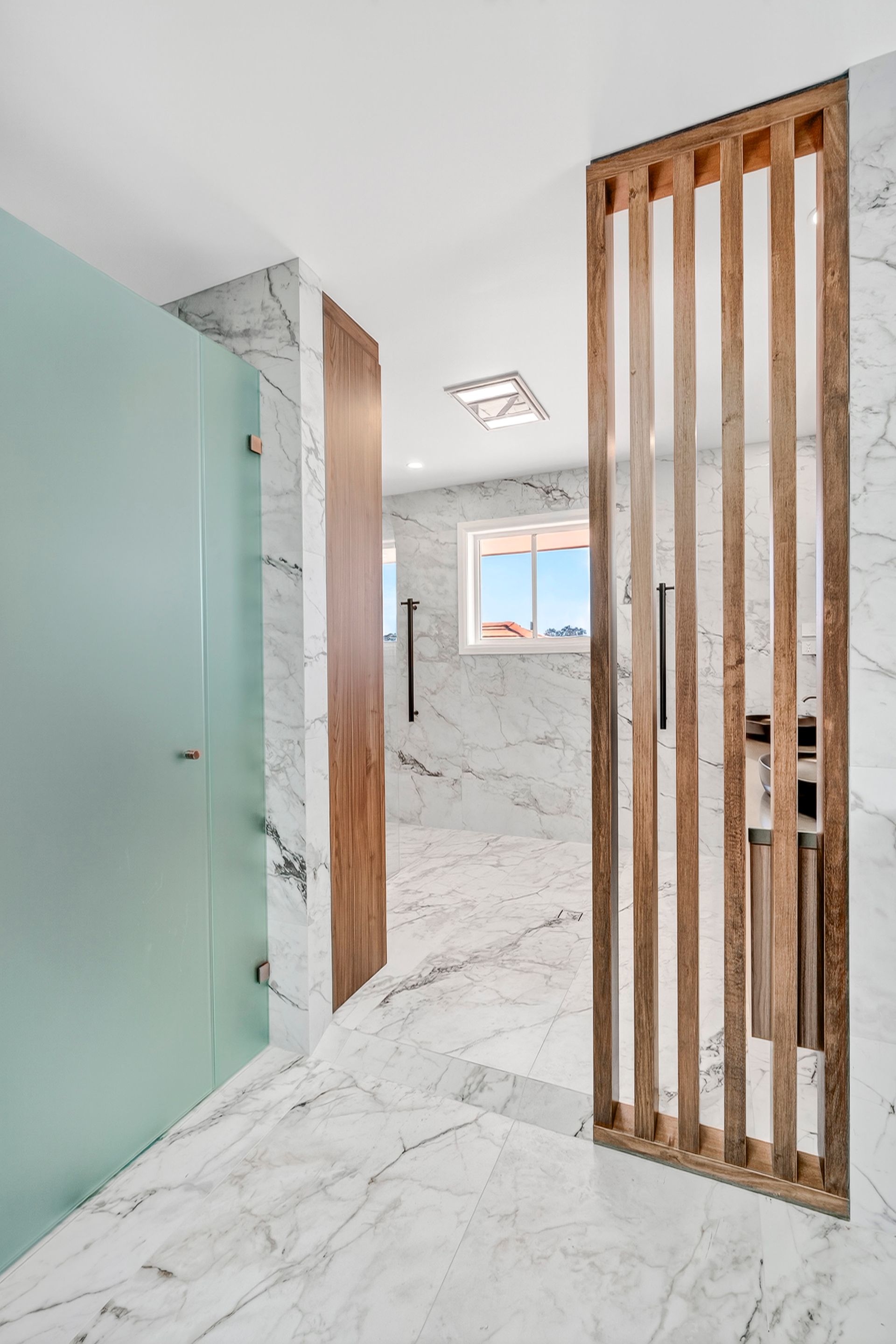 Modern bathroom with marble floors and walls, frosted glass shower, and wood slat divider — PK4 Projects in Port Macquarie, NSW