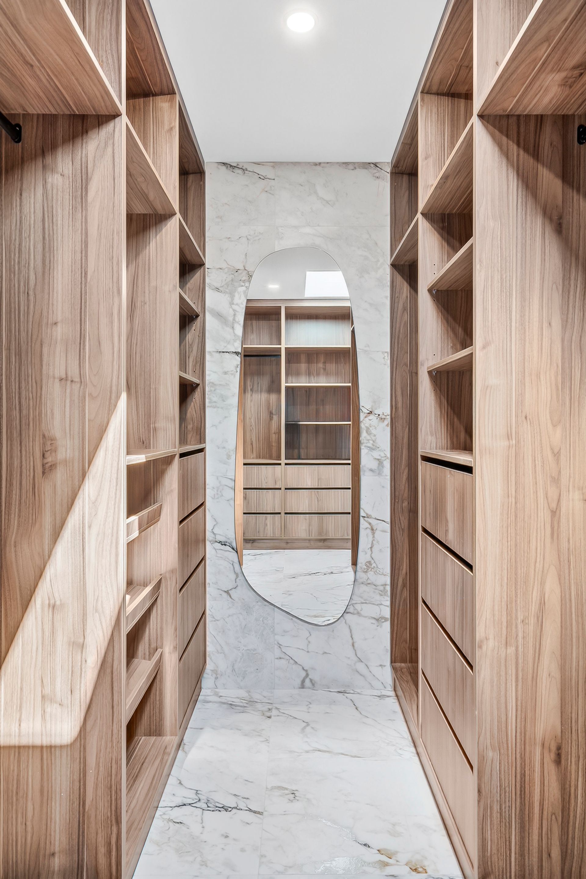 Walk-in closet with wooden shelving, marble walls and floor, and an oval mirror at the end — PK4 Projects in Port Macquarie, NSW