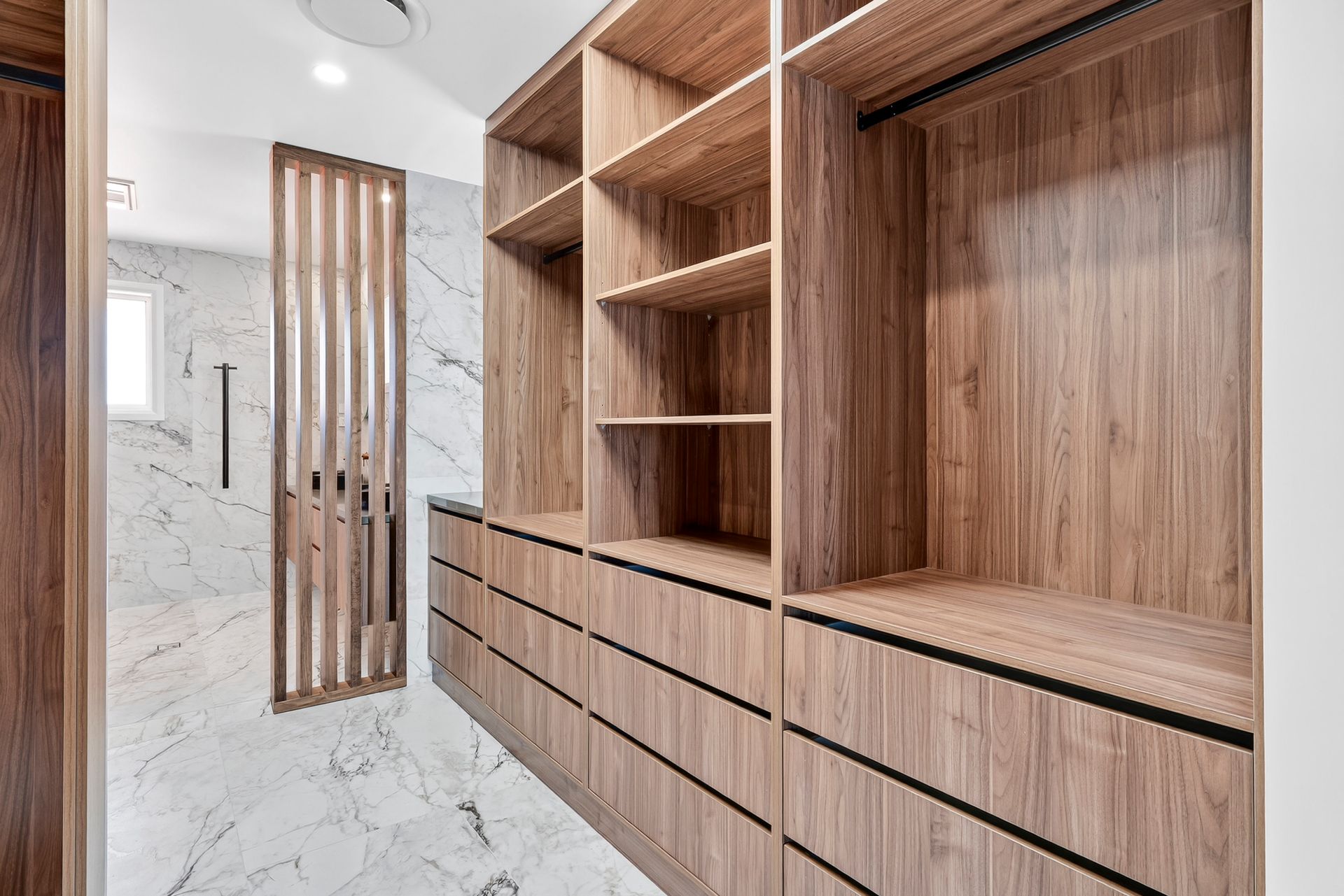 Walk-in closet with wooden shelves, drawers, and marble tile flooring.  Bathroom area with decorative wooden screen — PK4 Projects in Port Macquarie, NSW
