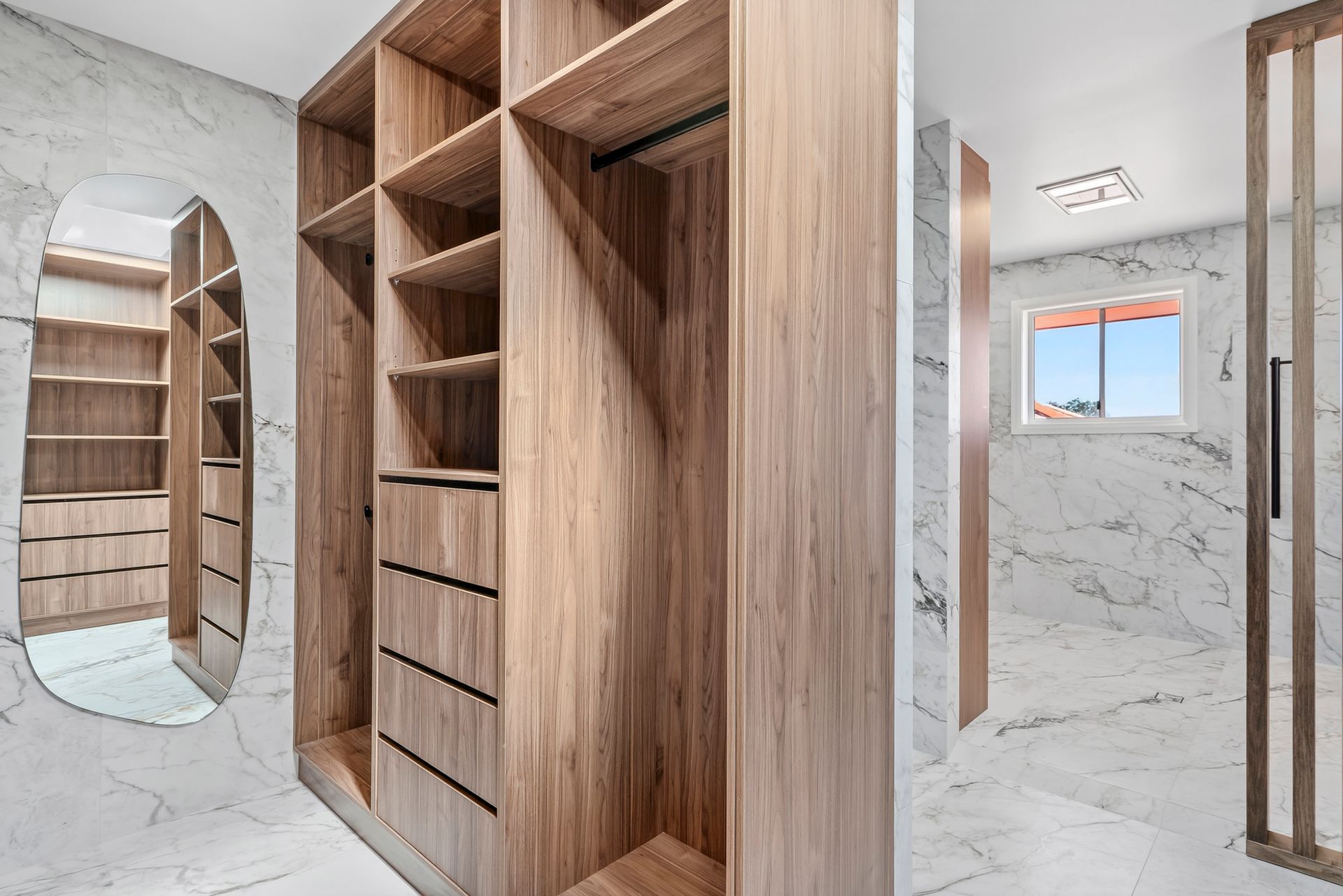 Walk-in closet with light wood shelving, white marble walls, and a large oval mirror — PK4 Projects in Port Macquarie, NSW