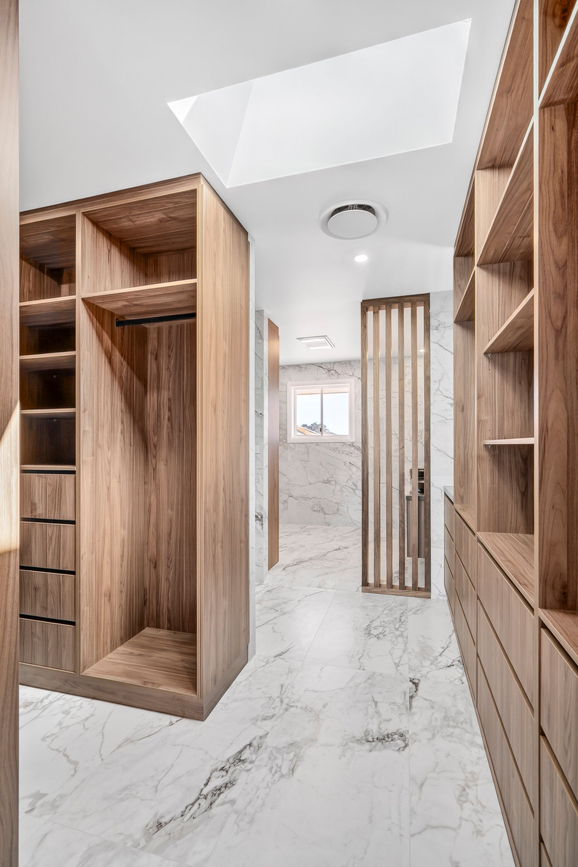 Wooden walk-in closet with shelves and drawers, marble flooring, and access to a bathroom — PK4 Projects in Port Macquarie, NSW