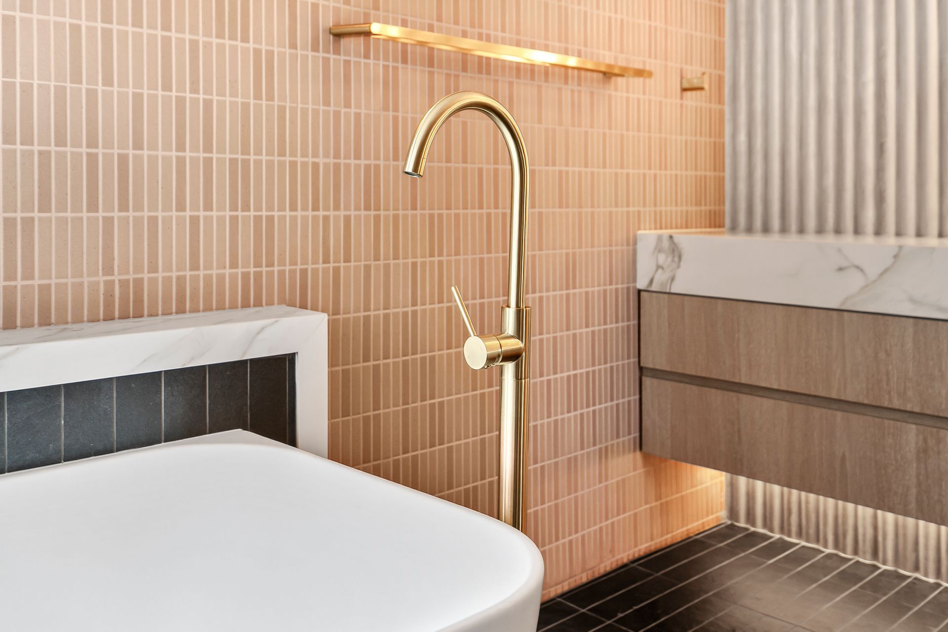 Gold faucet in a bathroom with pink tiled wall, a white bathtub, and wood cabinets  — PK4 Projects in Port Macquarie, NSW