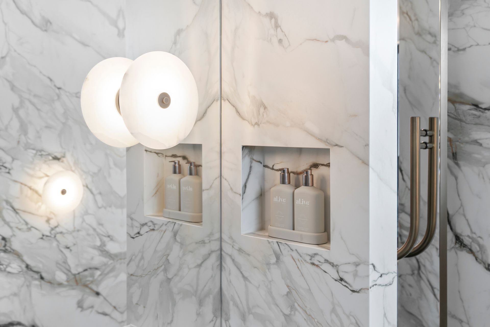 Marble-tiled shower with built-in shelves holding bottles. Round, glowing lights illuminate the space — PK4 Projects in Port Macquarie, NSW