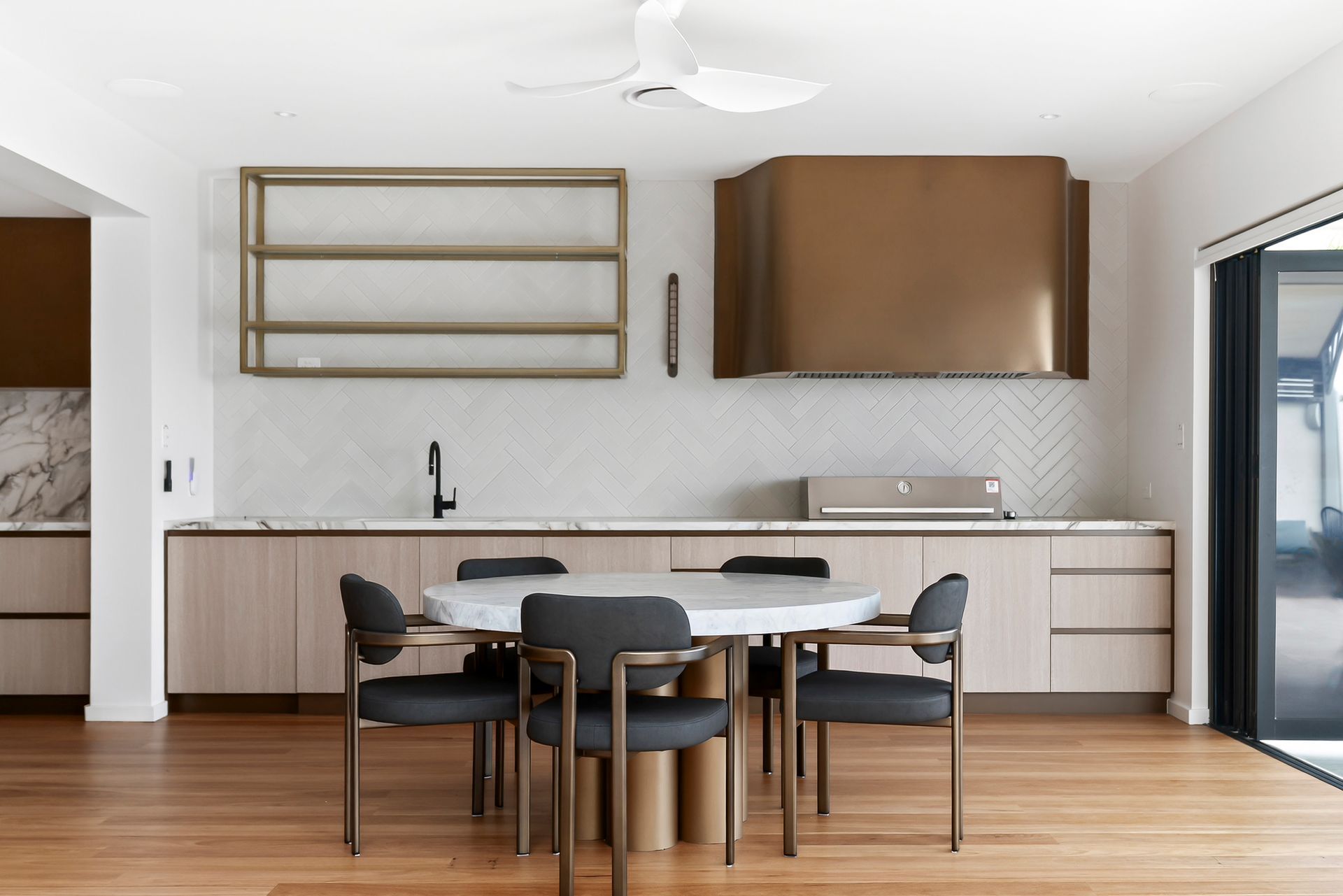 Modern kitchen with round table, chairs, brass range hood, light wood cabinets, and herringbone backsplash. — PK4 Projects in Port Macquarie, NSW
