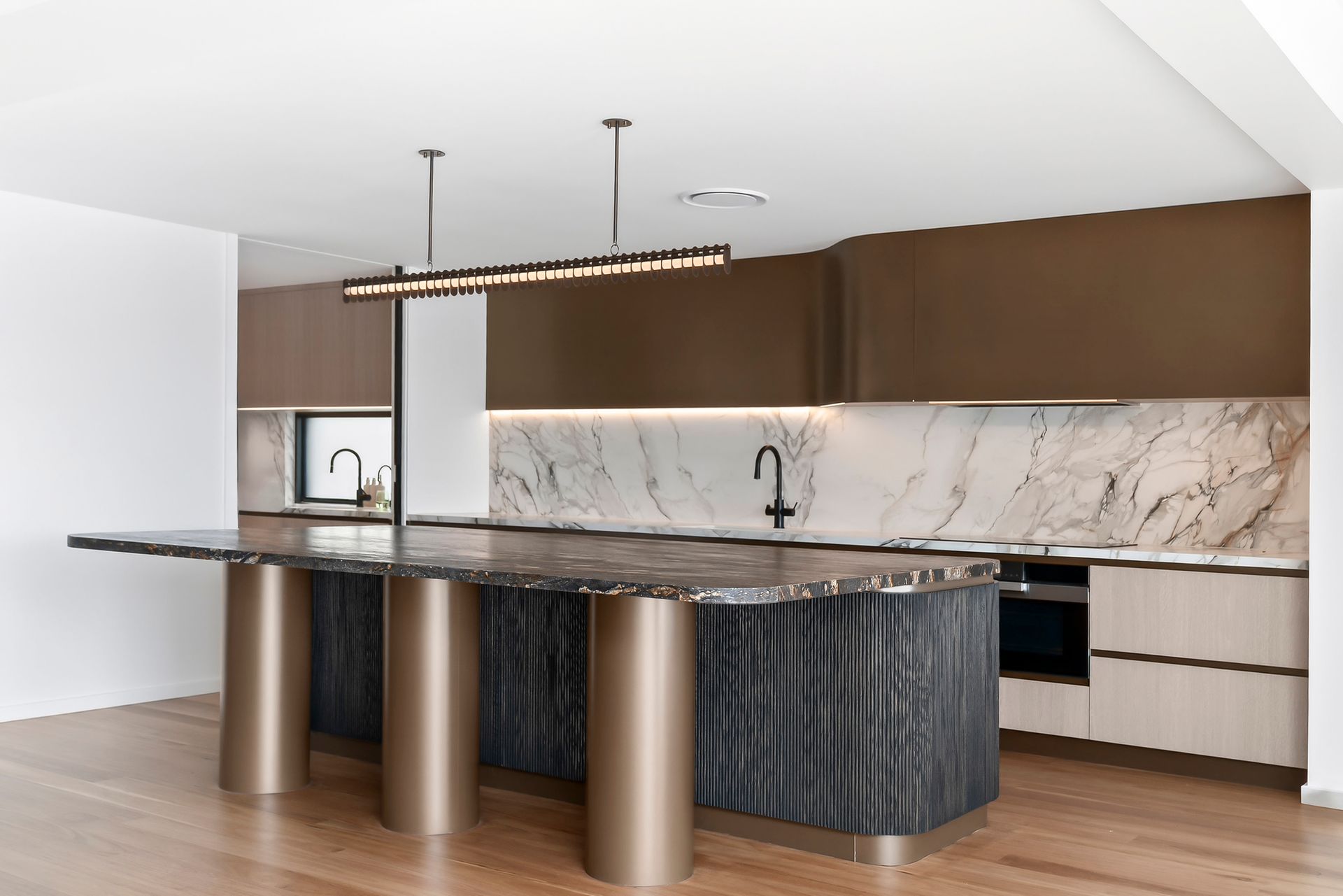 Modern kitchen with a marble island and brown cabinets, accented by a long linear light fixture — PK4 Projects in Port Macquarie, NSW