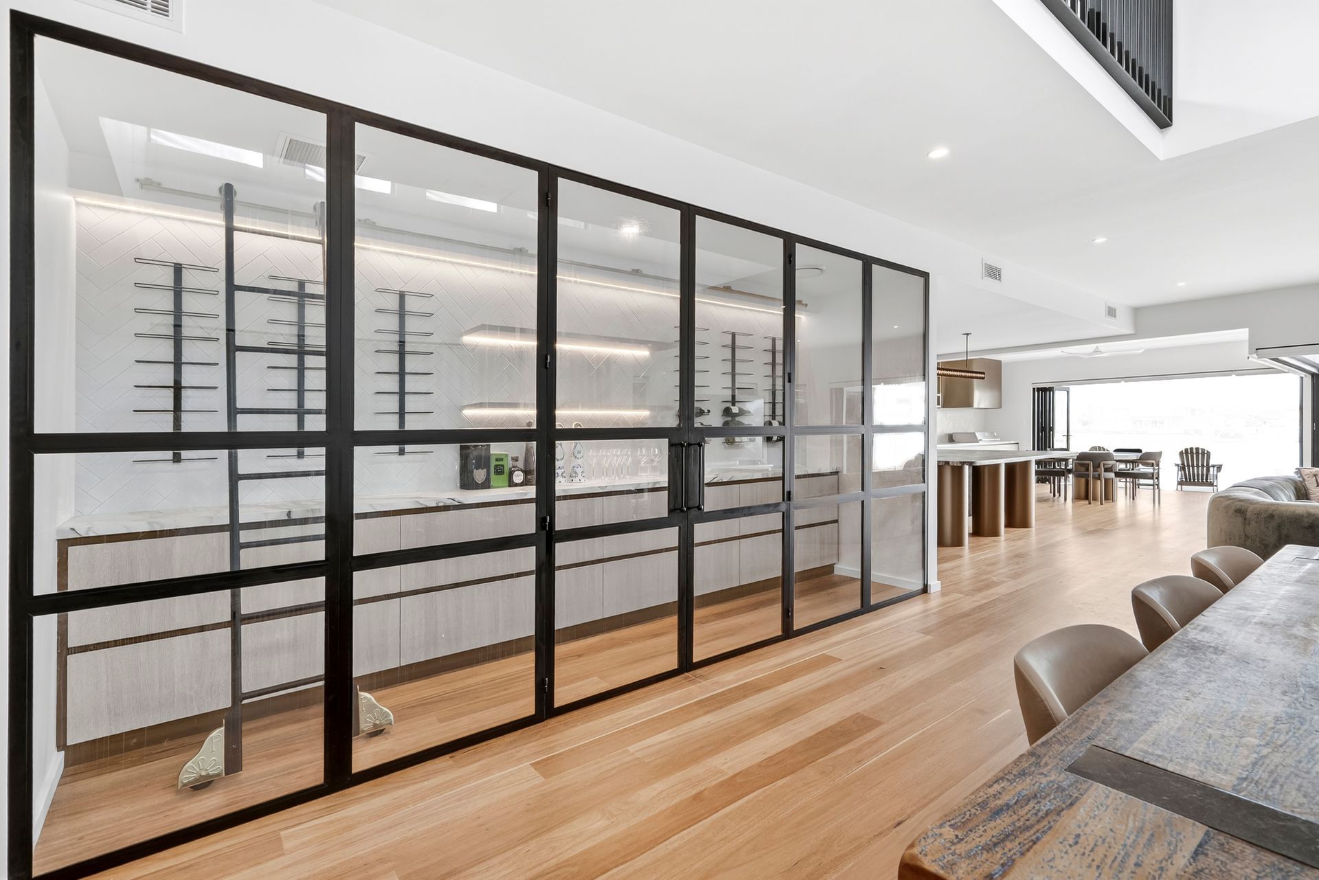 Glass-walled wine cellar with black metal framing in a modern living space with wood flooring — PK4 Projects in Port Macquarie, NSW
