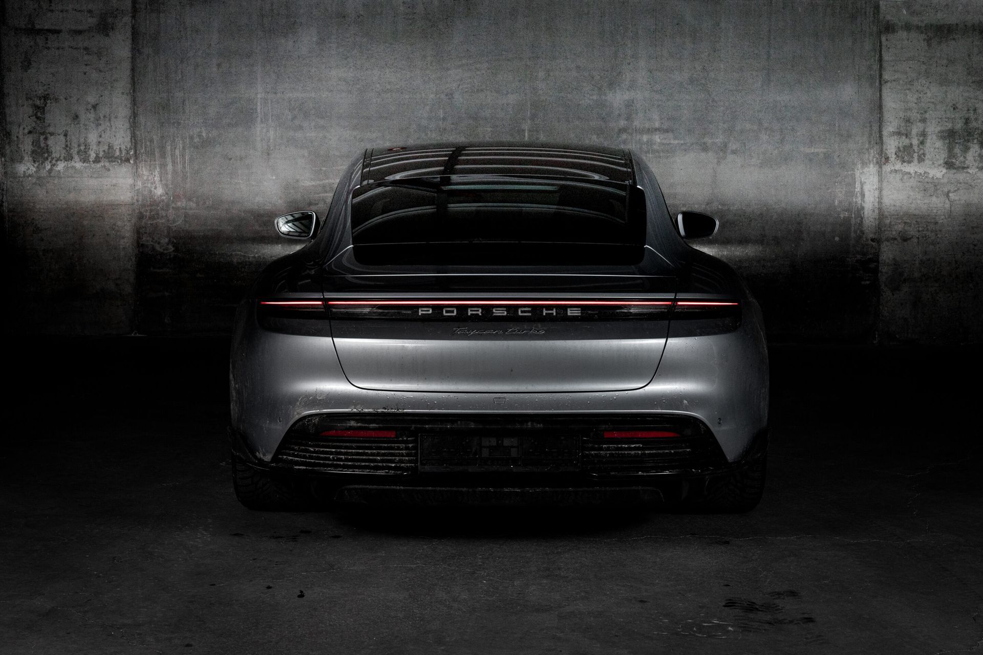 A silver porsche taycan is parked in a dark garage.