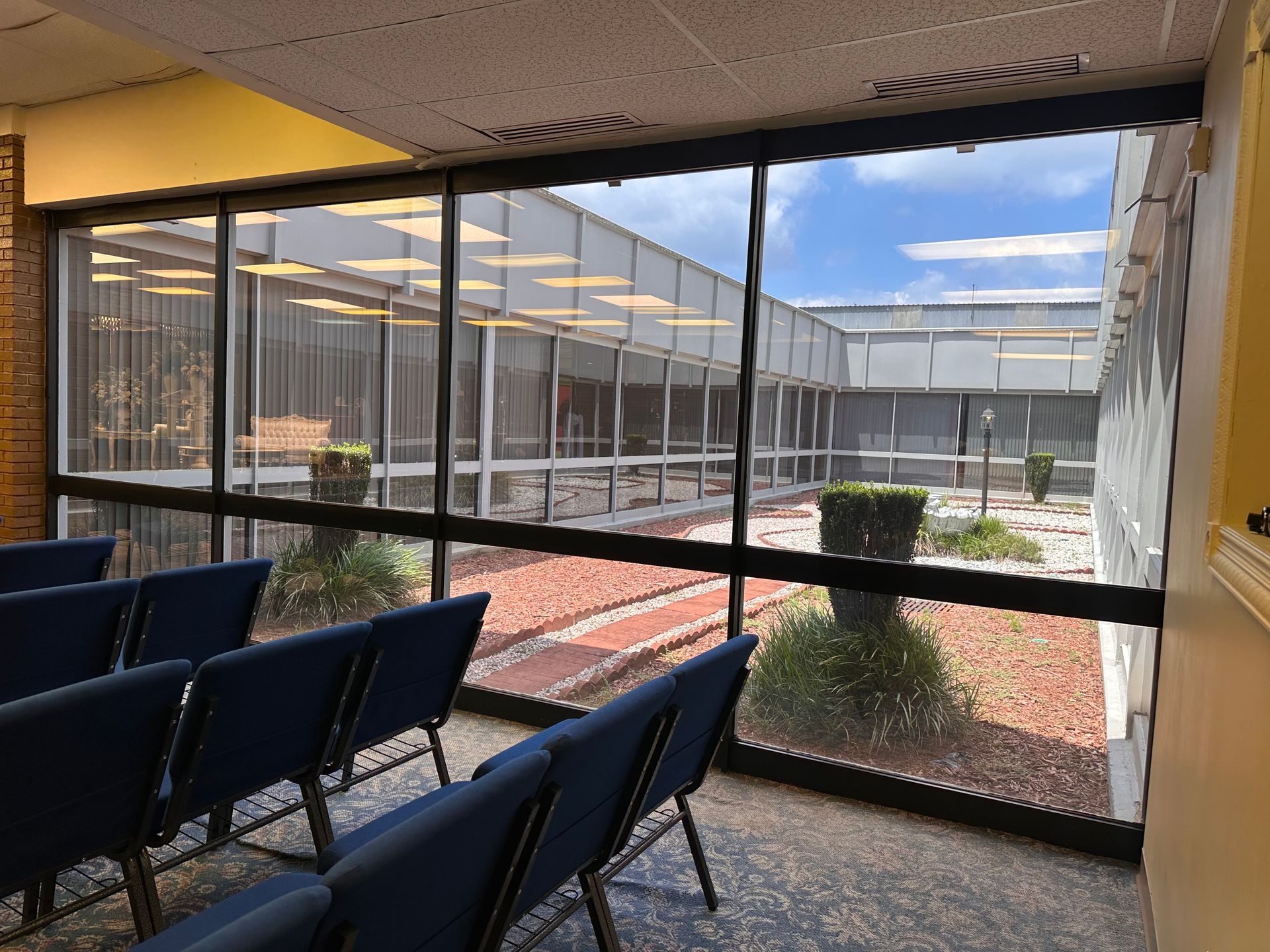 A covered patio with two sliding glass doors, wicker furniture, and an orange cushion. The stucco wall has decorative sconces.