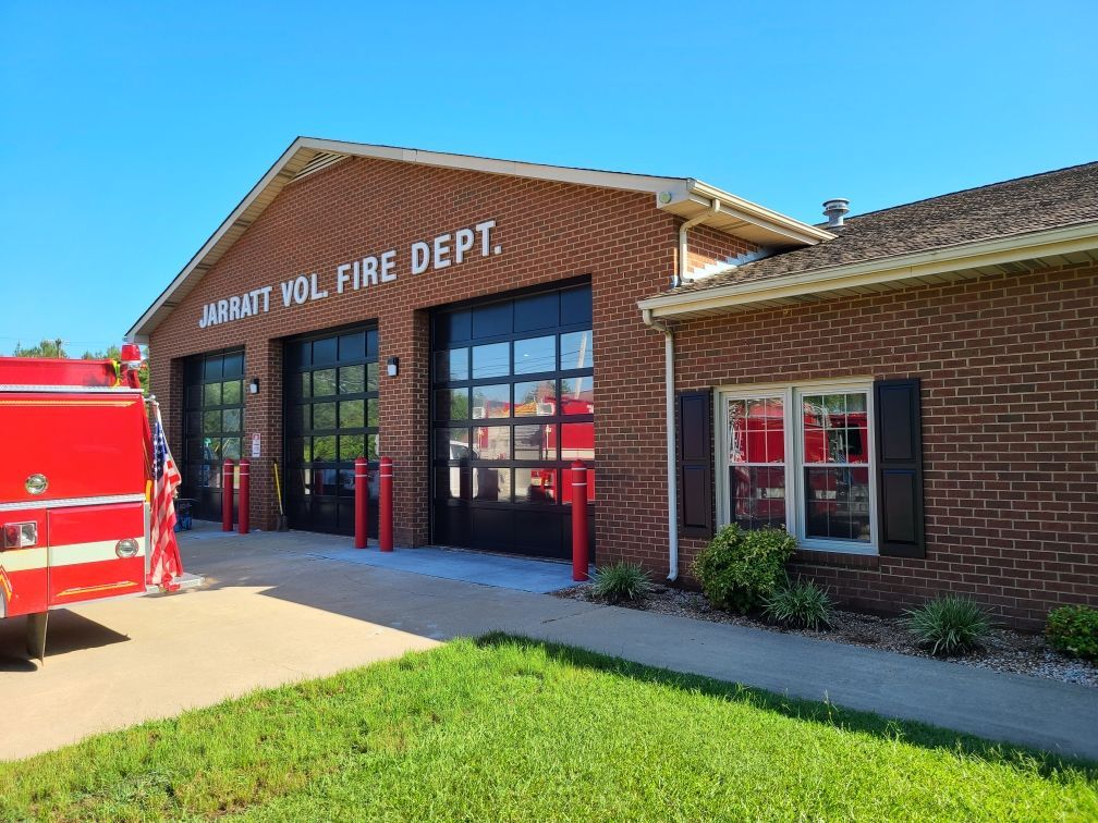 Exterior of Jarrett Vol. Fire Dept. building with red brick, three garage bays, and a firetruck. Blue sky overhead.