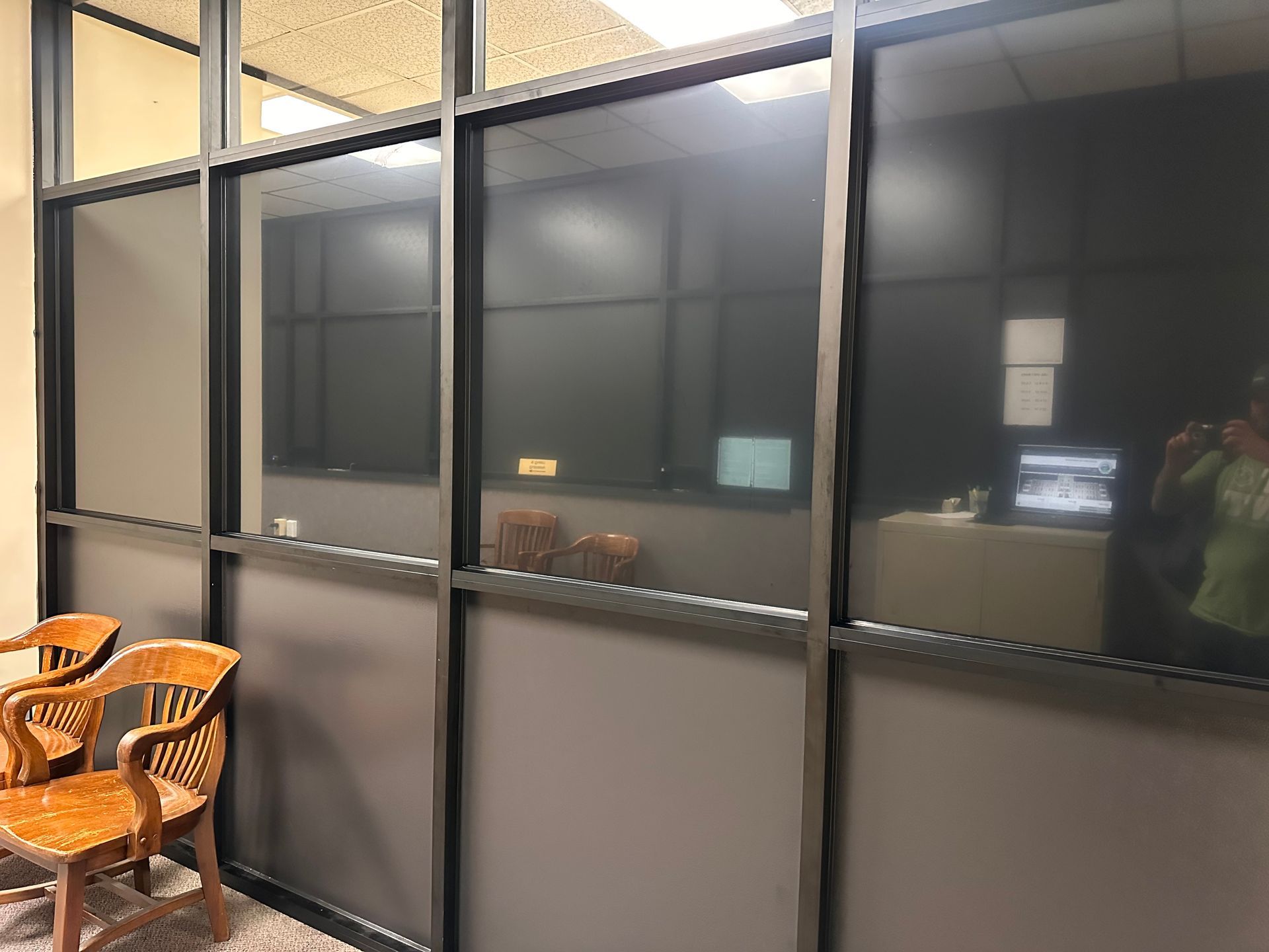 A waiting area with wooden chairs in front of a frosted glass wall. Offices are visible through the glass.