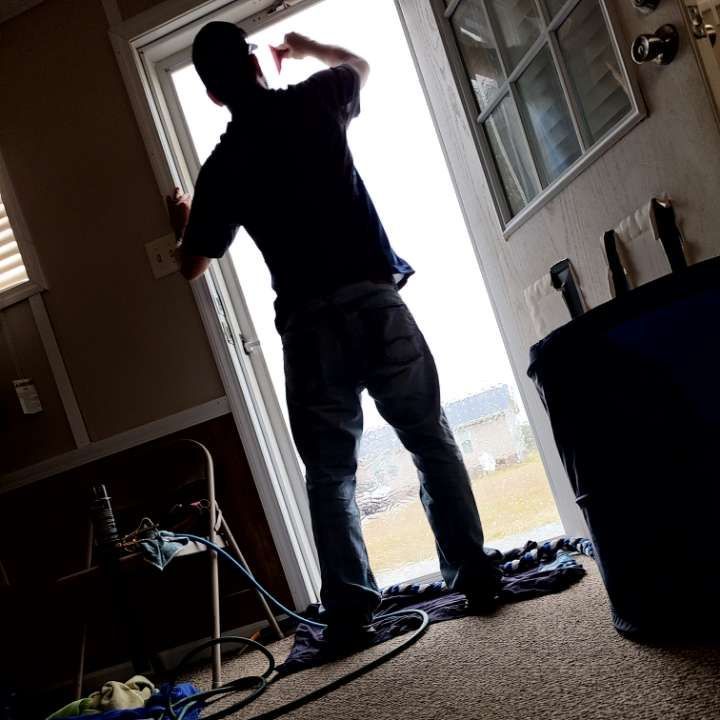 Person silhouetted in doorway, reaching up. Wearing dark shirt, jeans. Interior, light coming from outside.