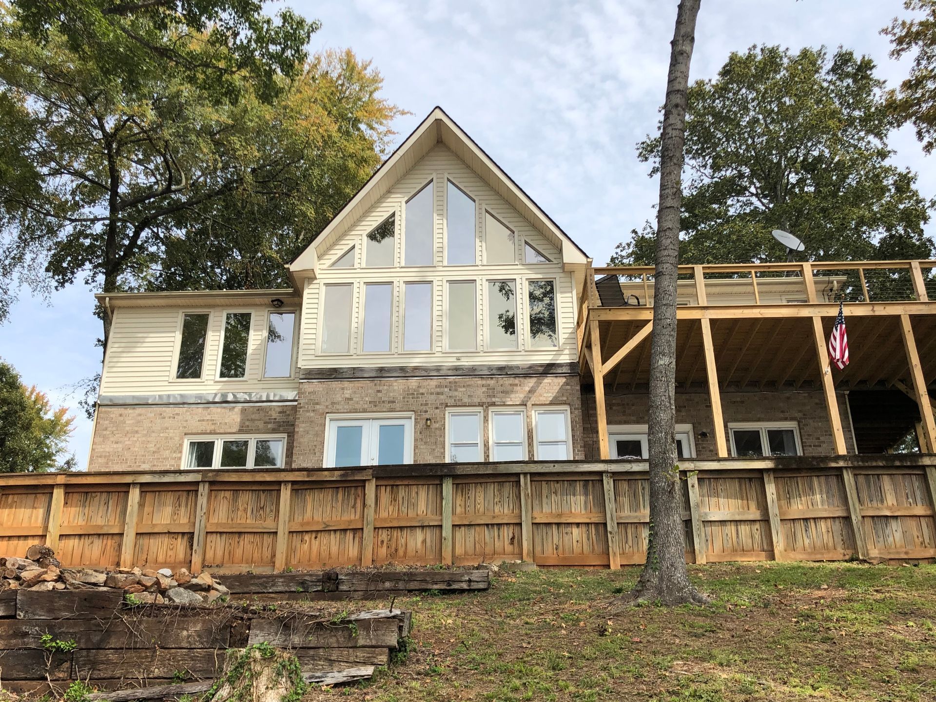 A two-story house with many windows, a deck, and a wooden fence, set amongst trees.