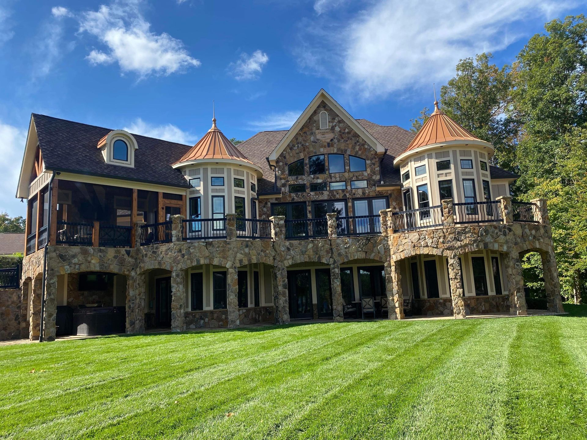 Large stone mansion with multiple levels and arched openings, featuring copper turrets and a manicured lawn against a blue sky.