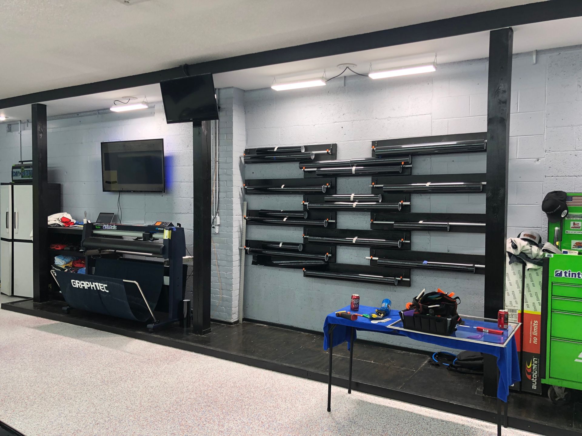 A garage interior with tools, a cutting machine, and shelves displaying automotive parts. A table with small items sits in the foreground.