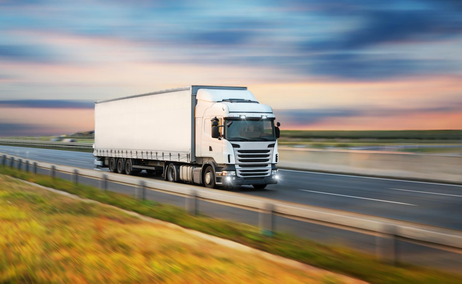 White semi-truck driving on a highway with blurred background of sky and land.