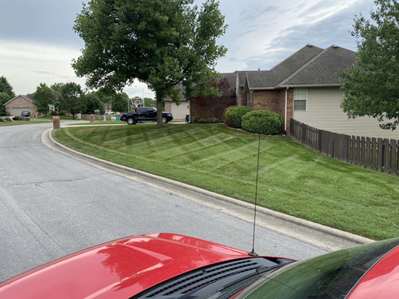 A red car is parked on the side of the road next to a lush green lawn.