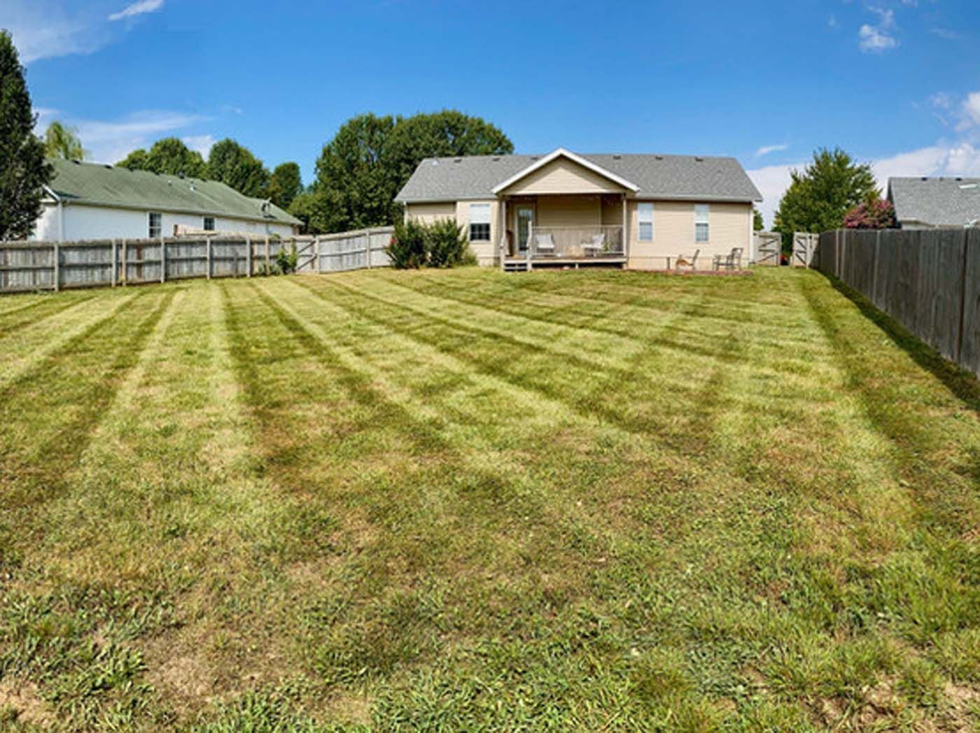 A backyard of a house with a fence and a lush green lawn.