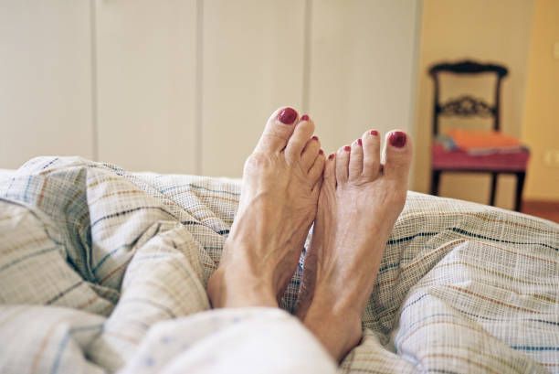 A woman 's feet are sticking out of the blankets on a bed.