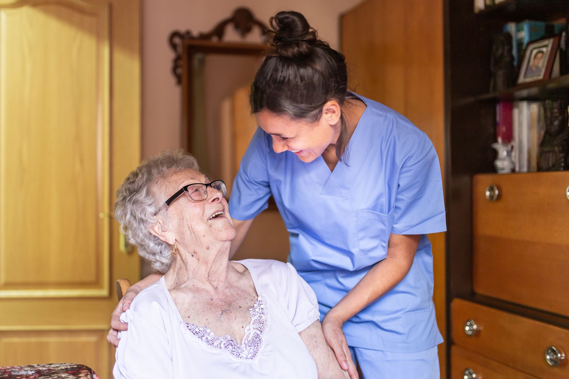 Happy senior woman laughing with her caregiver at home, enjoying quality home health care service.