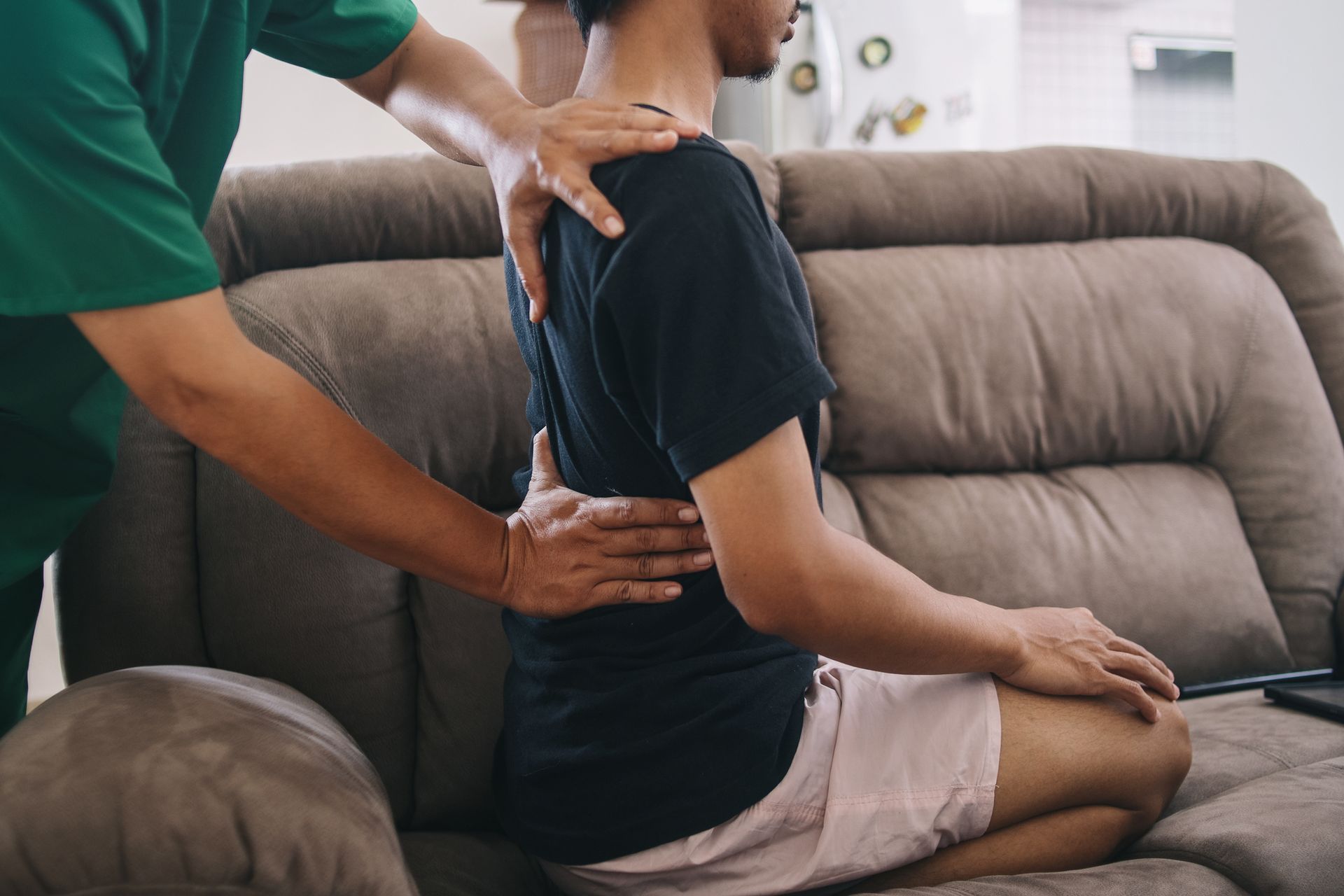 A person receiving a back adjustment on a couch.  Chiropractor in green shirt, patient in black tee.