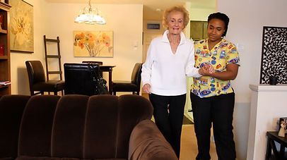 Elderly woman, with support, walking indoors with caregiver.