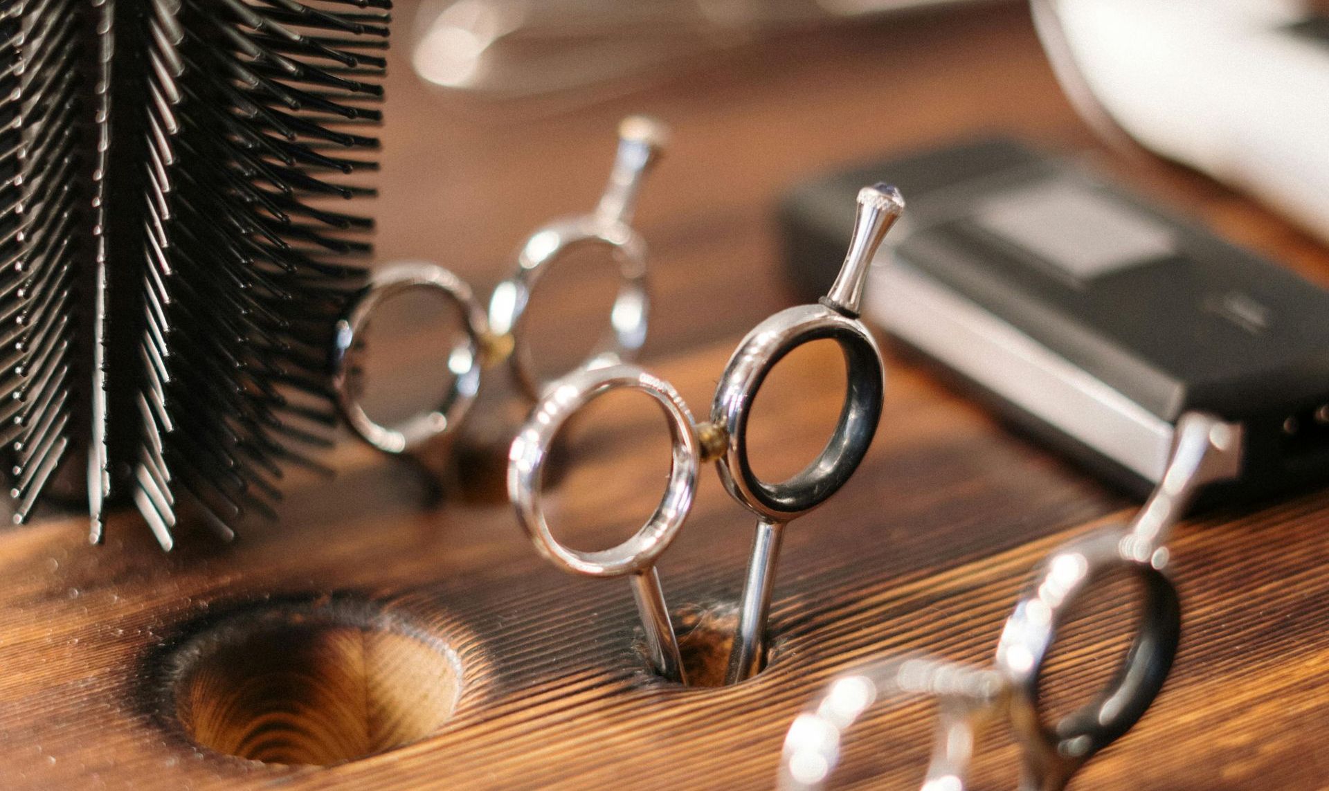 A pair of scissors sitting on top of a wooden table next to a brush.