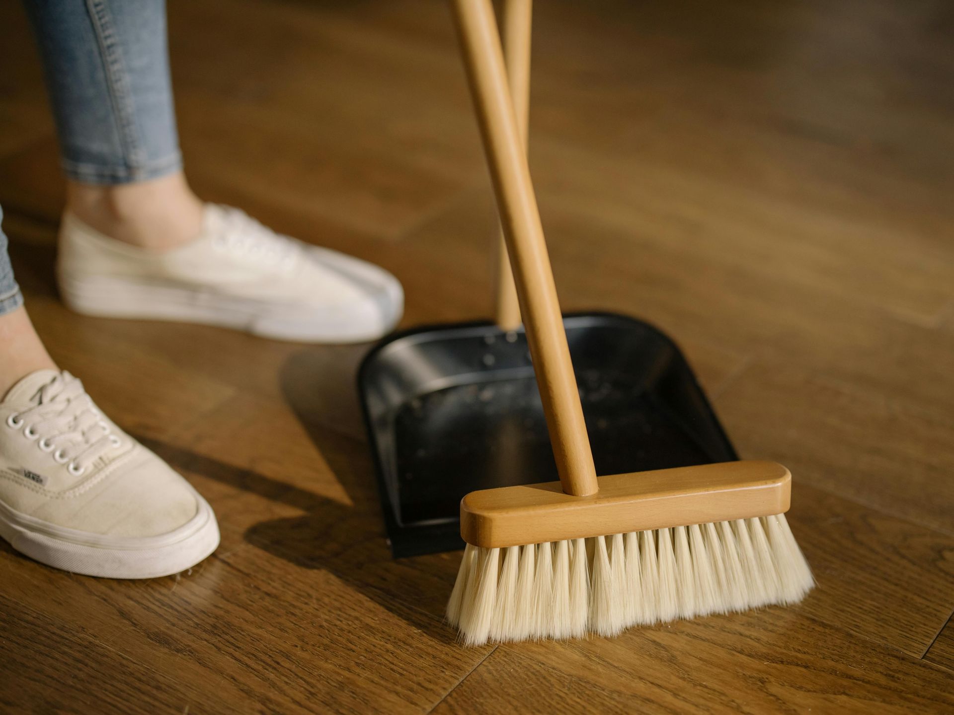 A person is cleaning the floor with a broom and shovel.