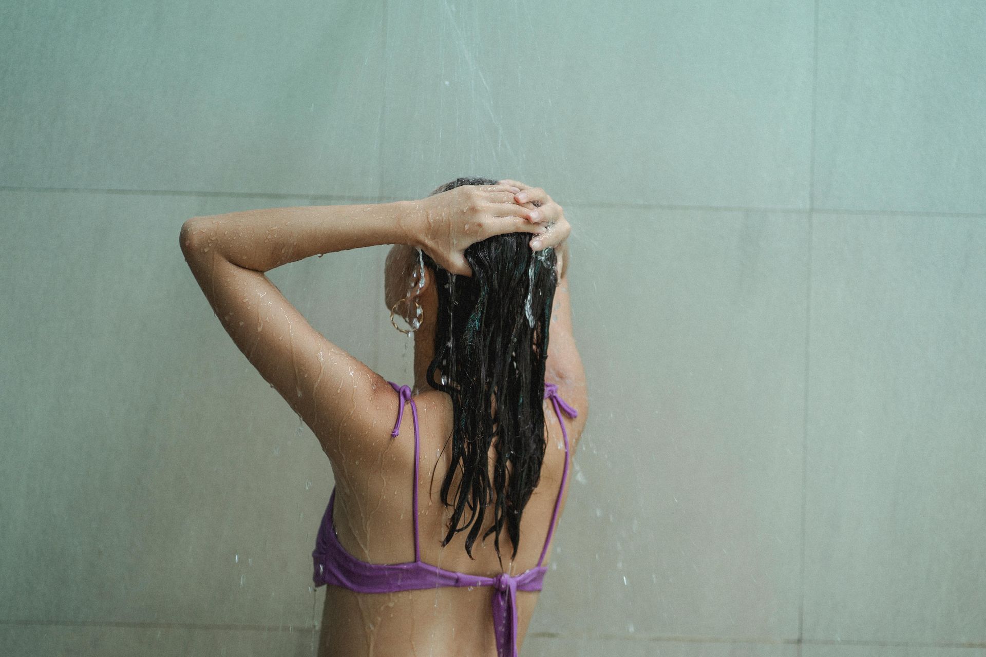 A woman in a bikini is taking a shower and washing her hair.