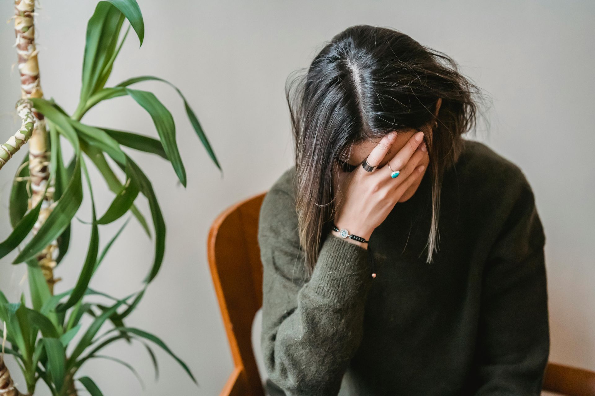 A woman is sitting in a chair covering her face with her hand.