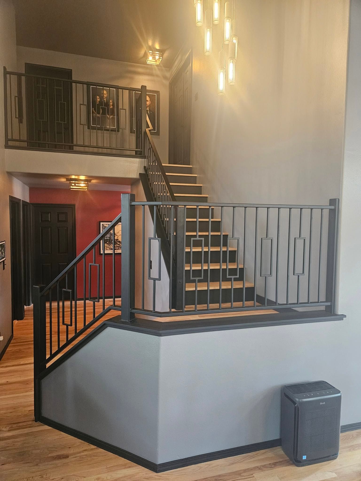 Interior staircase with black railings, warm wall lights, and a small trash bin beside the landing.