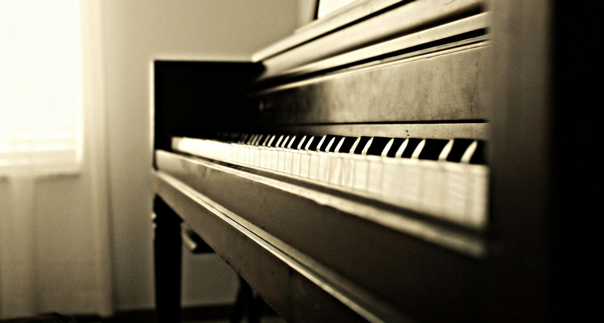 A piano is sitting in a room next to a window.