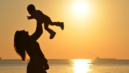 a woman is holding a baby in her arms on the beach at sunset .