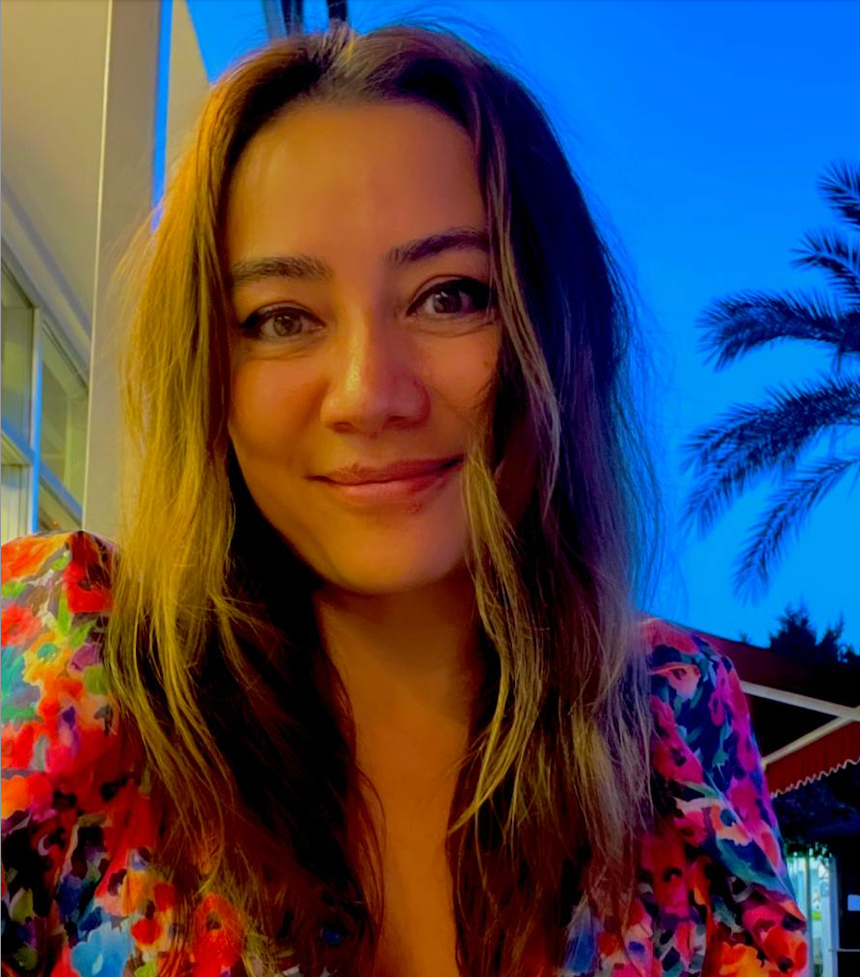 A man wearing a white sweater and a black vest has a backpack on his back