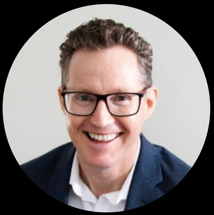 A woman in a black coat is standing in front of a bridge.