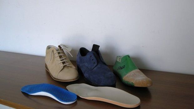 Su un tavolo sono disposte diverse paia di scarpe, tra cui modelli beige, blu scuro e verdi con solette sciolte.