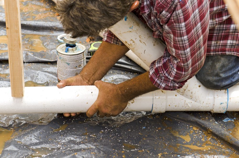 A Man In A Plaid Shirt Is Working On A Pipe — Sampson Plumbing Pty Ltd In Currumbin, NSW