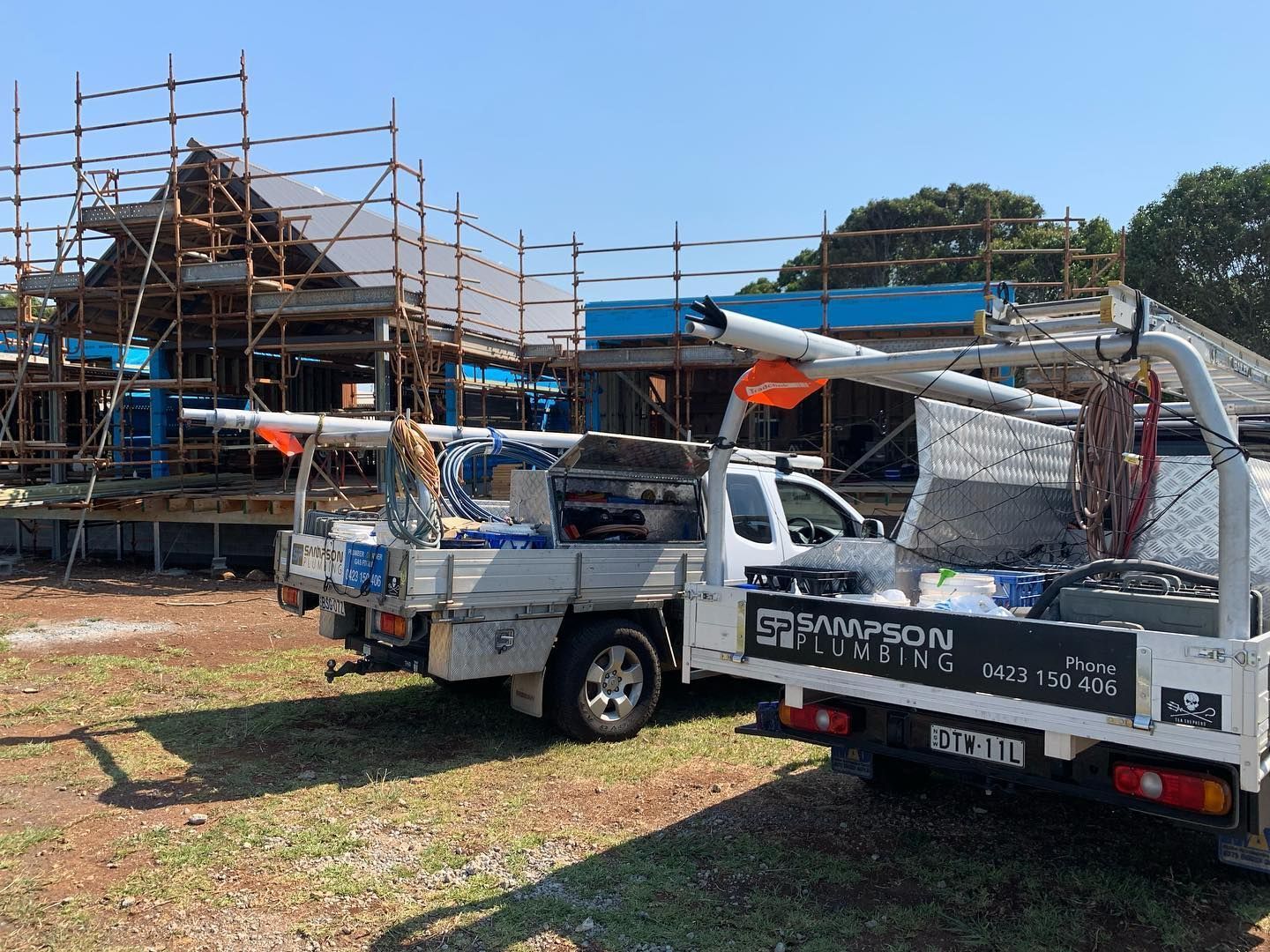 Two Construction Trucks Are Parked In Front Of A Building Under Construction — Sampson Plumbing Pty Ltd In Casuarina, NSW