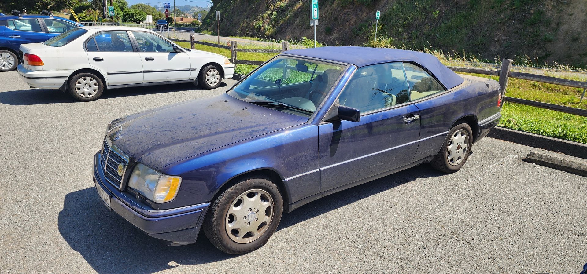 Blue sedan parked in a sunny lot, with a white car in the background.
