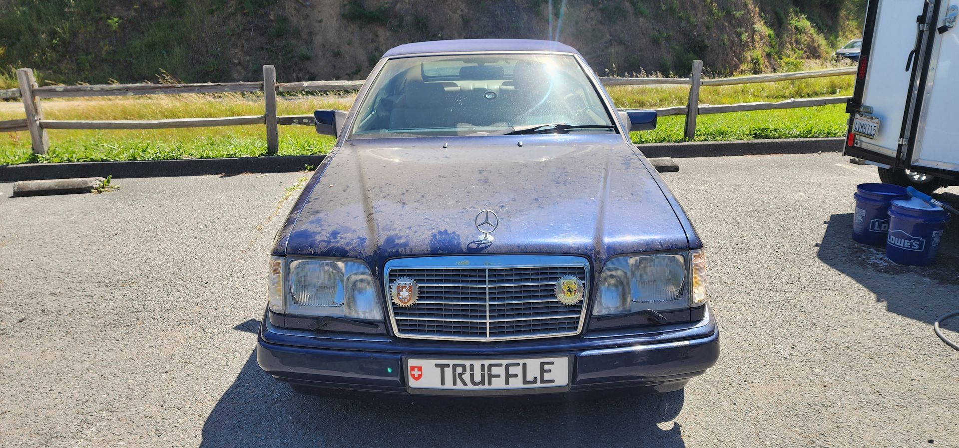 Blue vintage car parked on gravel, front view with a TRU FLE license plate and rural fence in the background