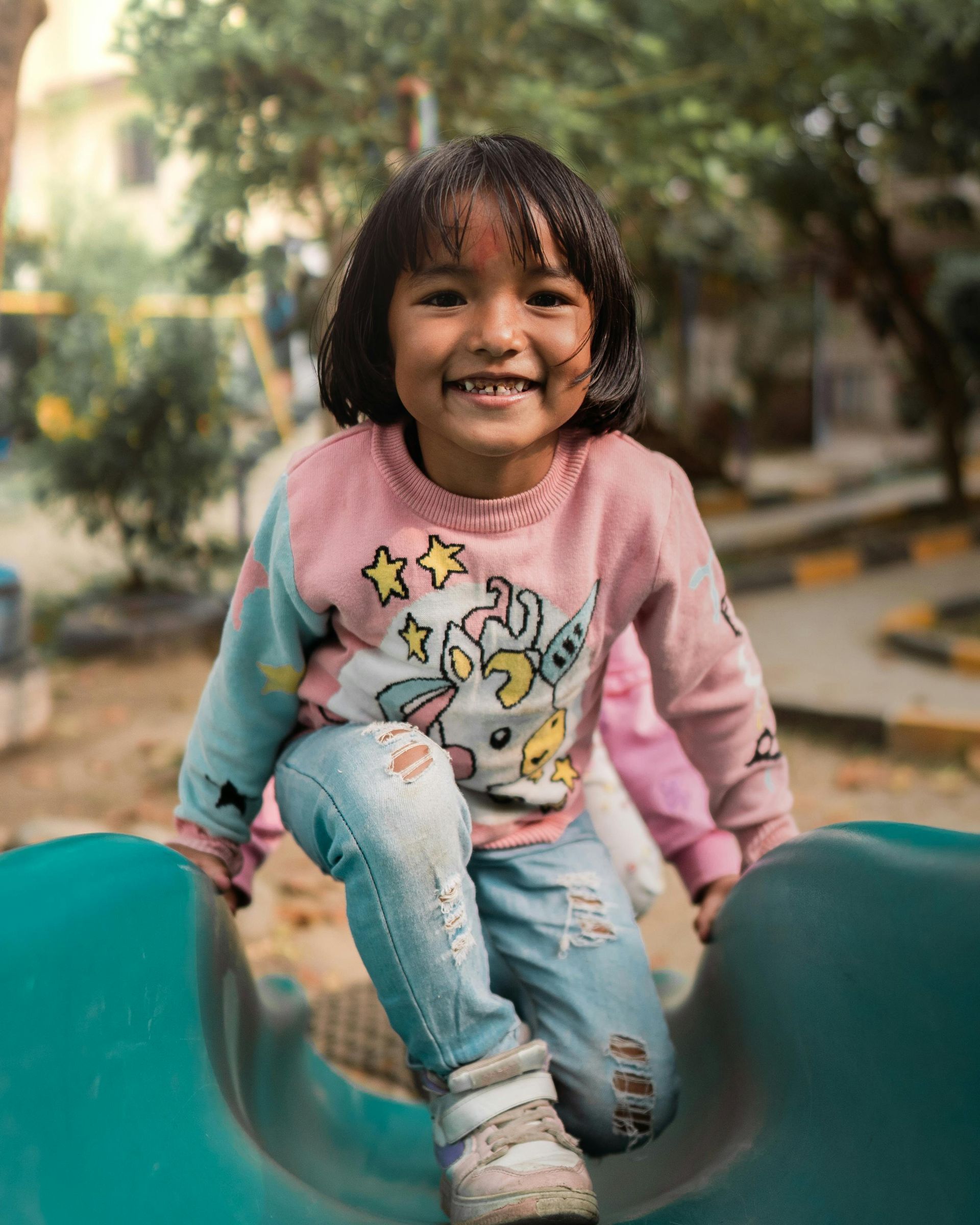 A little girl is sitting on a slide at a playground.
