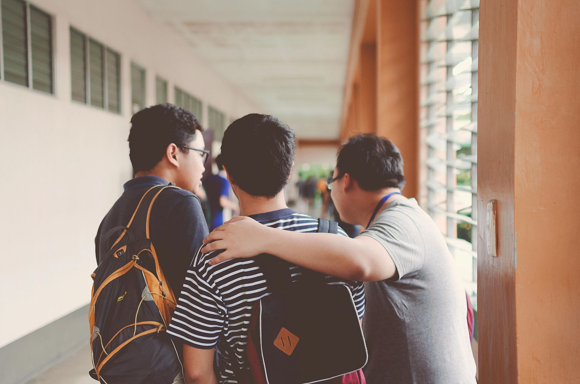Three young men in a school hallway, one with an arm around another's shoulder, talking.