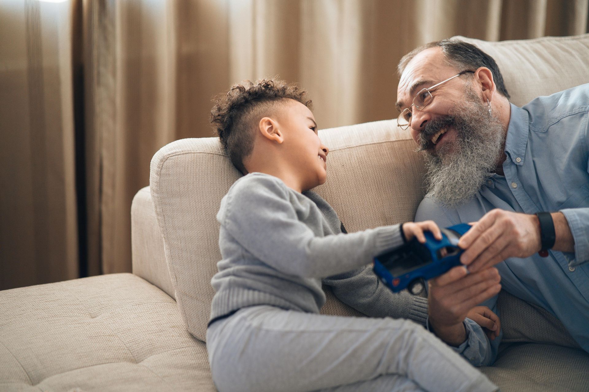 Boy and man on a couch playing with a blue toy car, smiling at each other.
