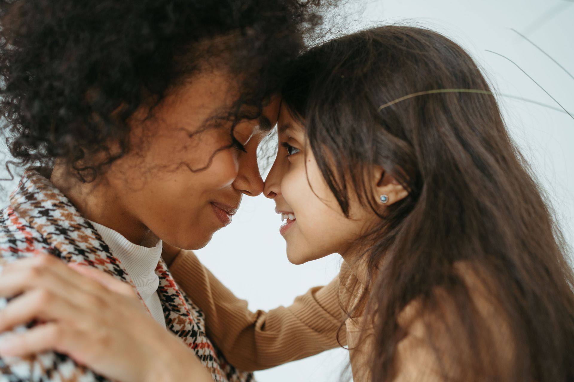 Two people lean forehead-to-forehead, smiling gently in a warm, close-up moment.